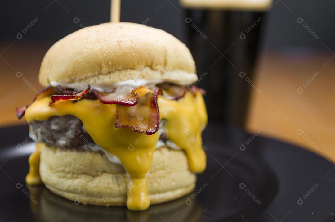 Hambúrguer de bacon caseiro e molho cheddar na mesa de madeira e fundo preto