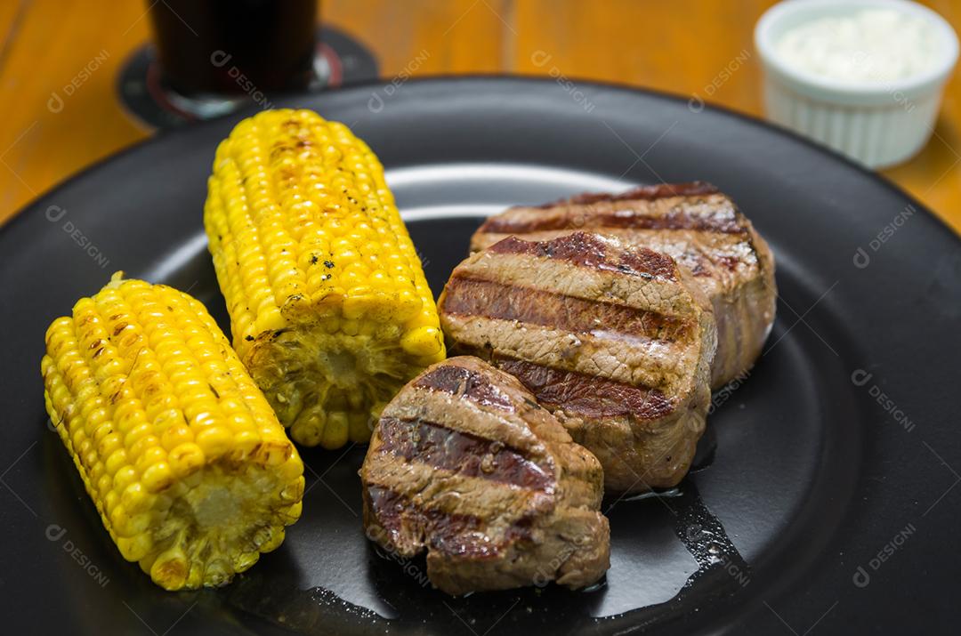 Delicioso de filé mignon com milho assado e copo de cerveja.
