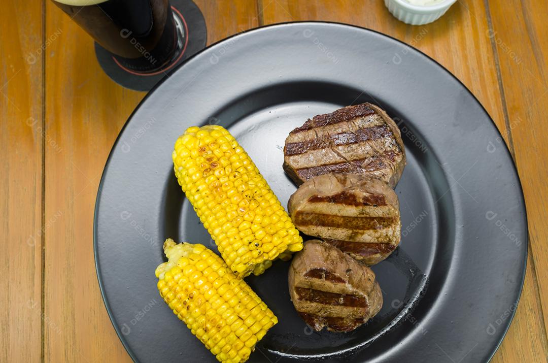 Delicioso de filé mignon com milho assado e copo de cerveja.