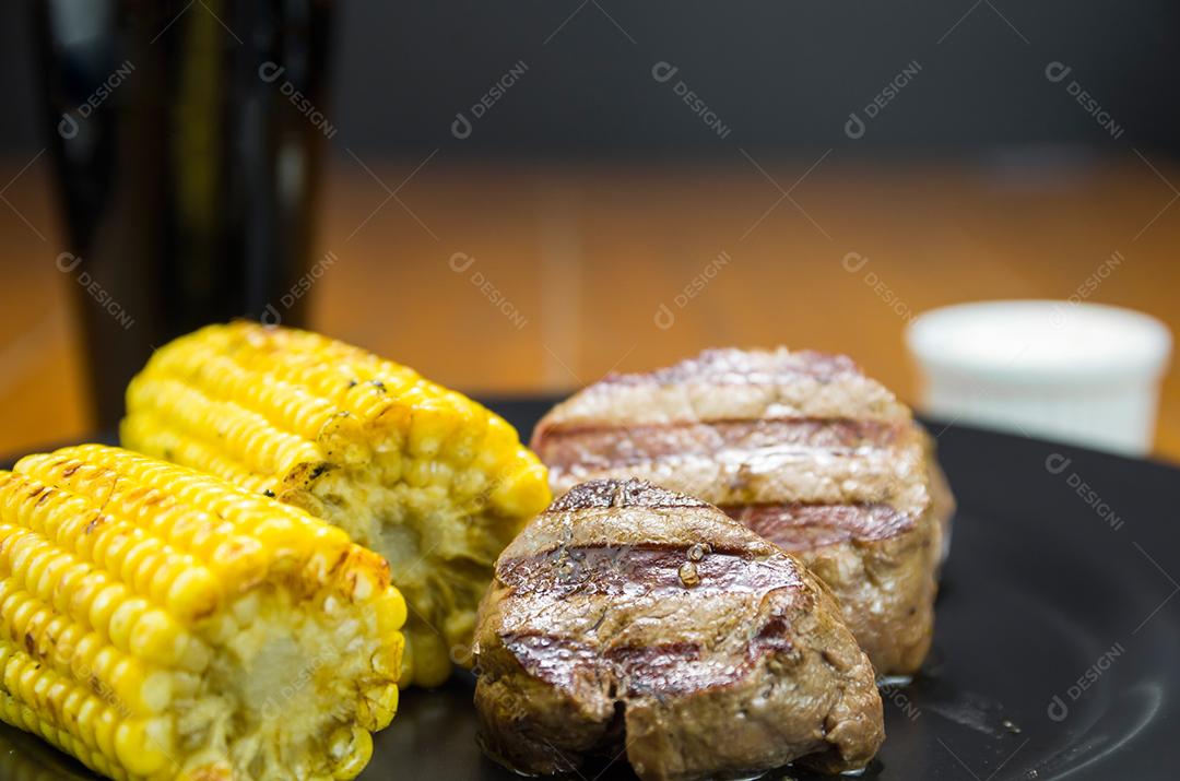 Delicioso de filé mignon com milho assado e copo de cerveja.