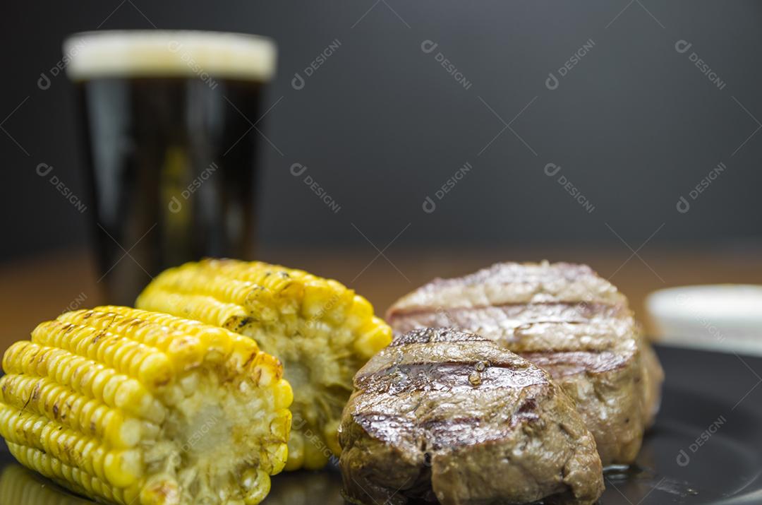 Delicioso de filé mignon com milho assado e copo de cerveja.