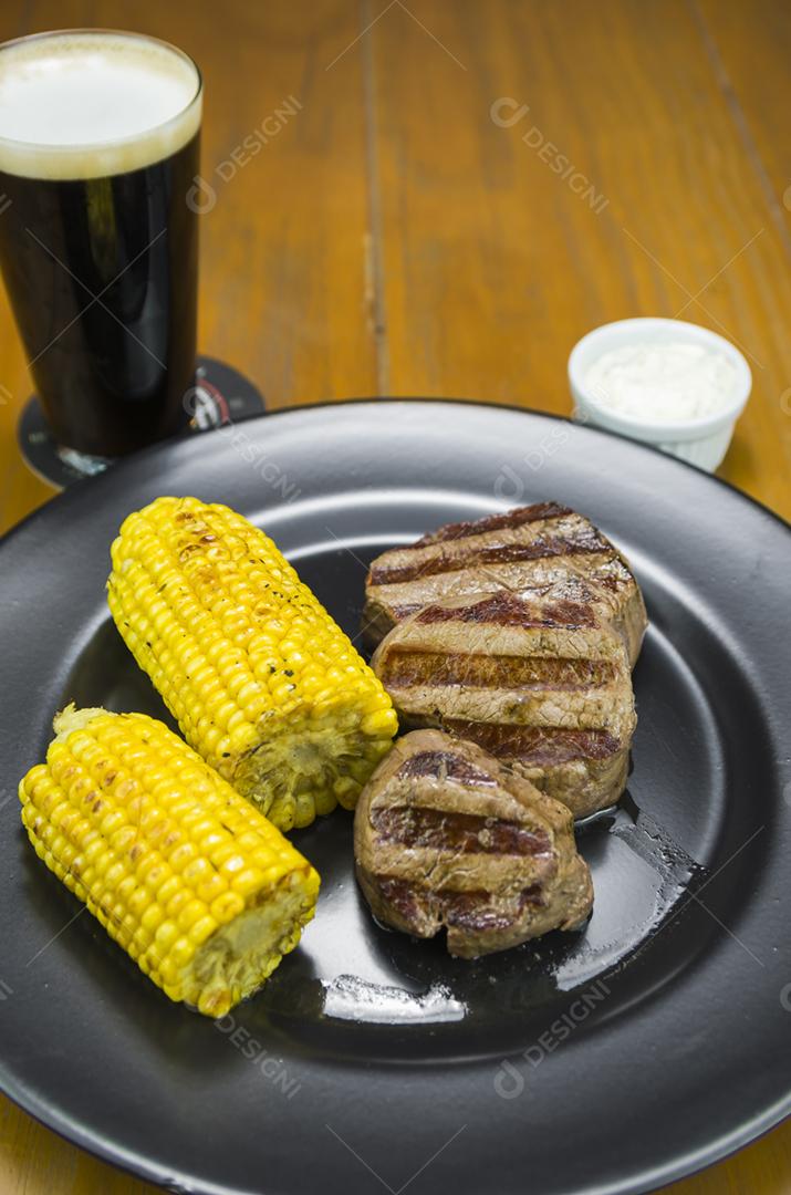 Delicioso de filé mignon com milho assado e copo de cerveja.