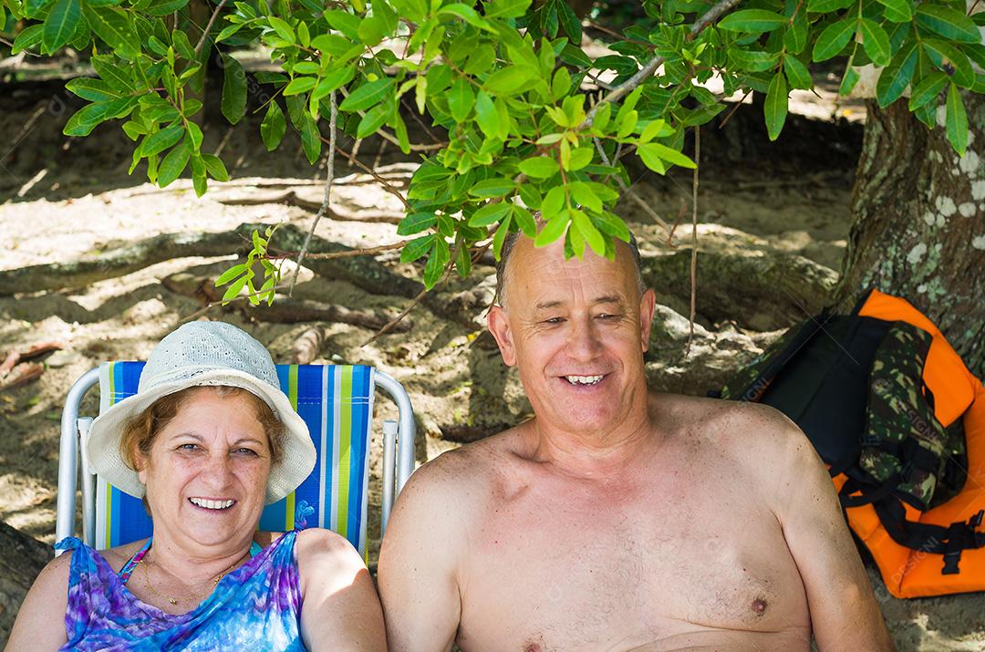 Casal de velhos rindo na praia, sentado, amor.
