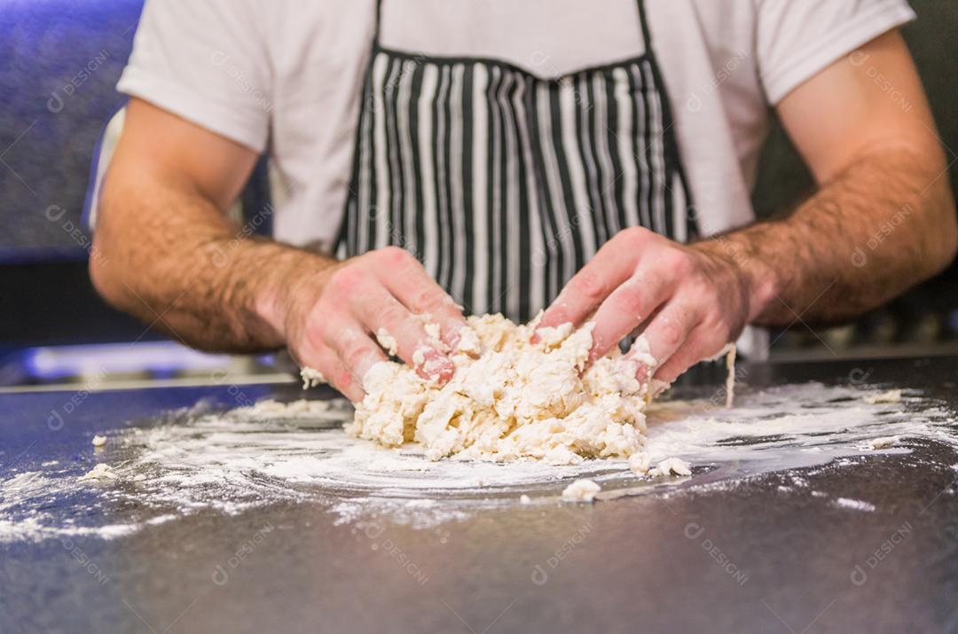 Homem preparando massa de pizza na mesa de granito preto