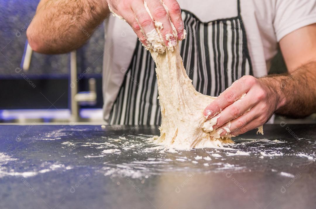 Homem preparando massa de pizza na mesa de granito preto