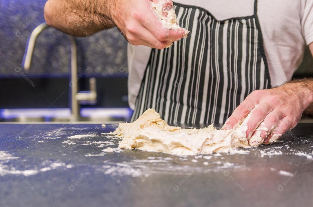 Homem preparando massa de pizza na mesa de granito preto