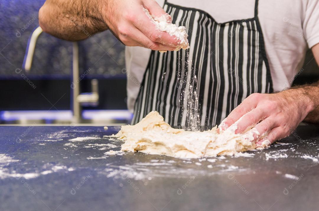 Homem preparando massa de pizza na mesa de granito preto