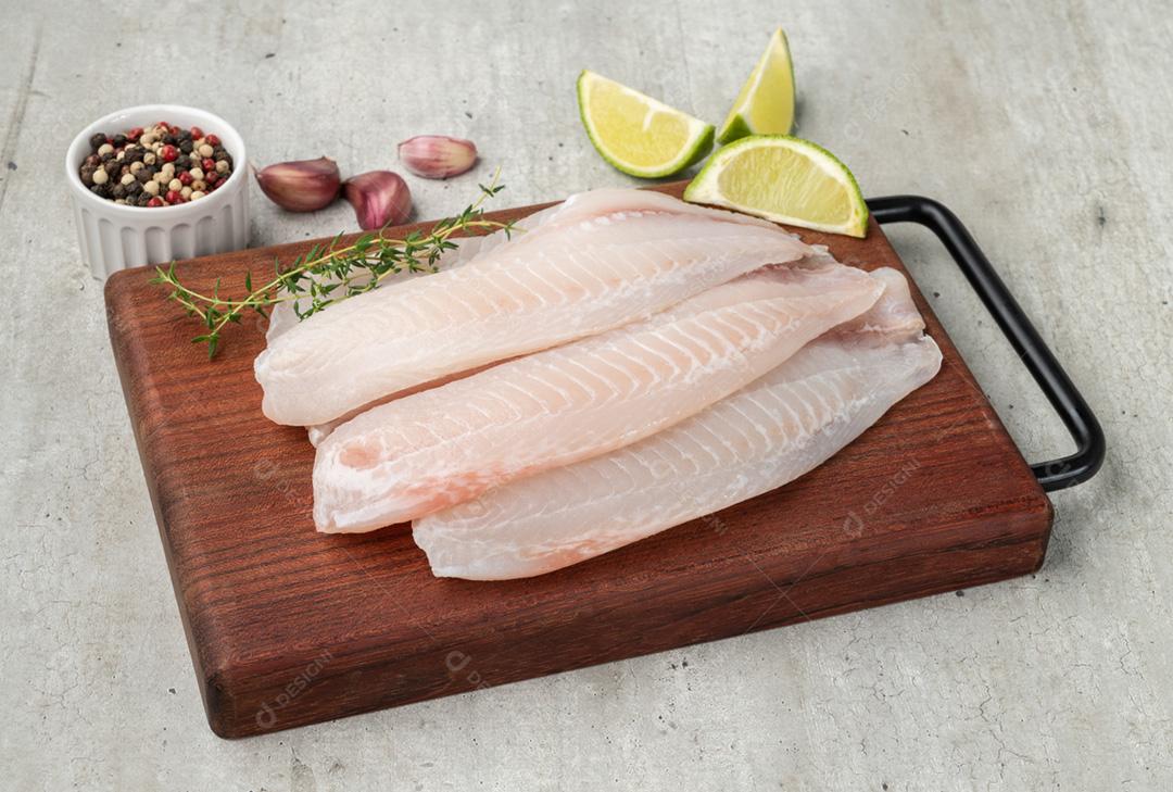 Filé de peixe tilápia cru com temperos sobre mesa de madeira com c