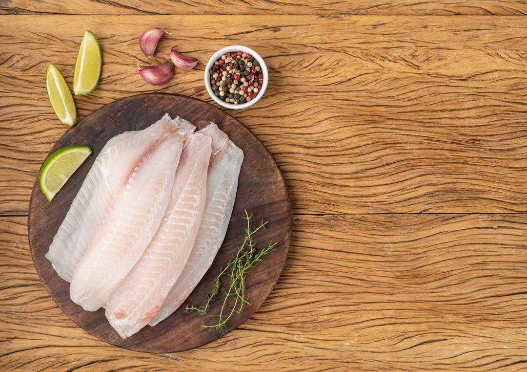 Filé de peixe tilápia cru com temperos sobre mesa de madeira com c
