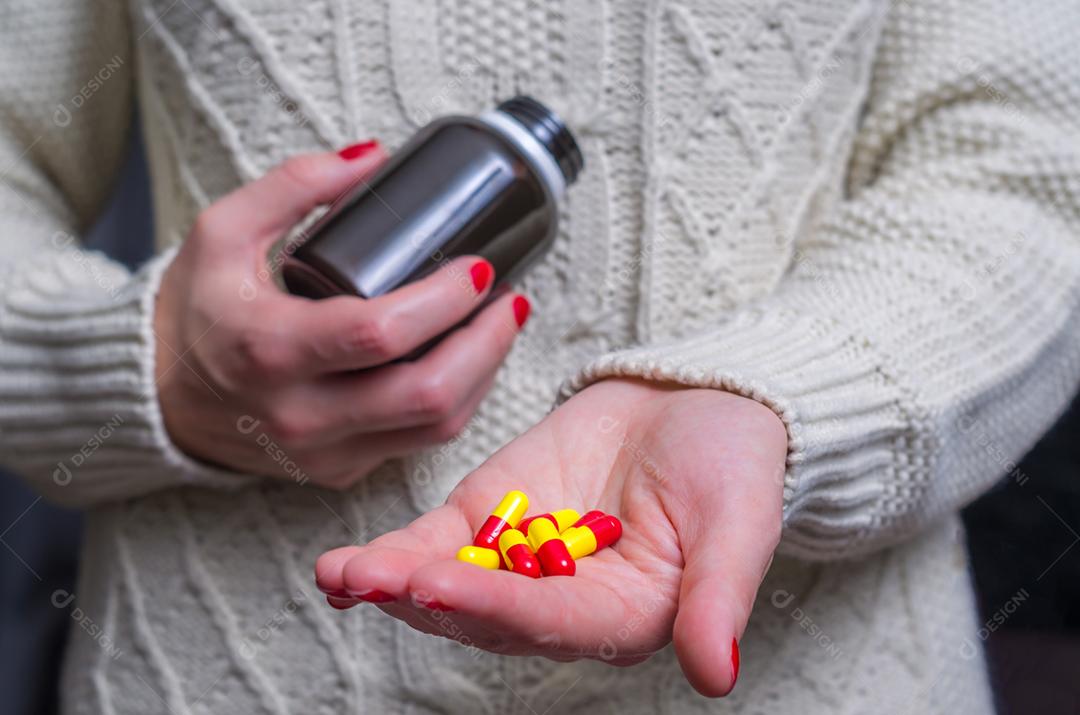 Mulher vestida com roupas de inverno com pílulas de medicamentos. pílulas na mão mulher com gripe