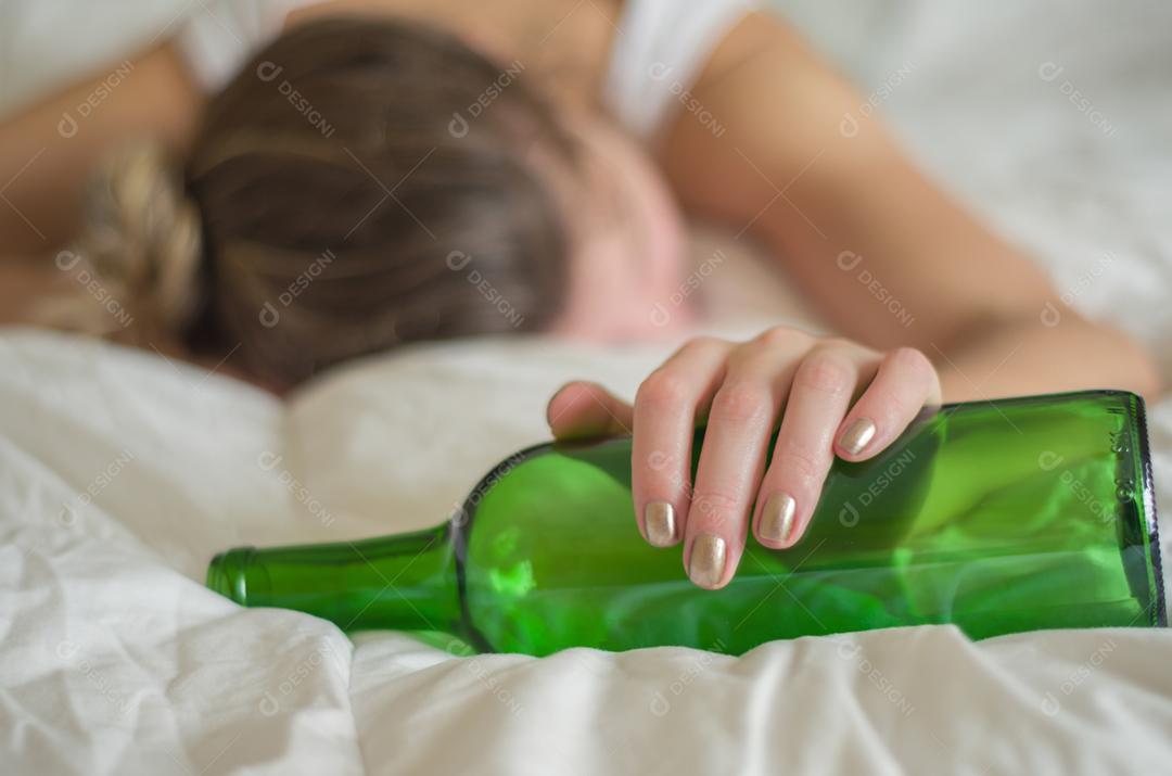 Grande conceito de abuso de álcool. Jovem, cabelos loiros, desmaiou na cama depois de beber muito álcool.