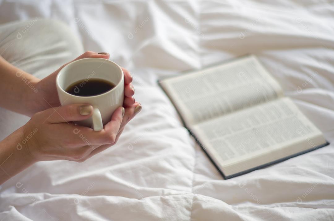 Mulher com pernas cruzadas, lendo livro e bebendo café. Visto de cima lateralmente.