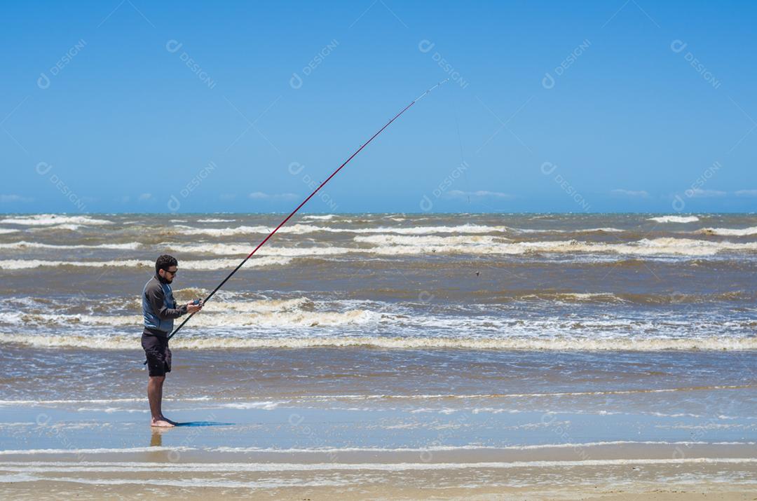 Jovem pesca na praia, pesca esportiva.