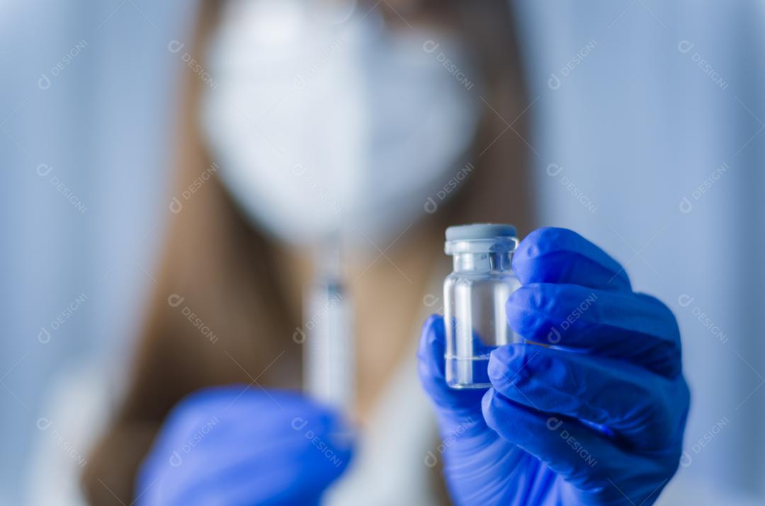 Female doctor with stethoscope on shoulder holding syringe and COVID-19 vaccine. Health and medical concept.