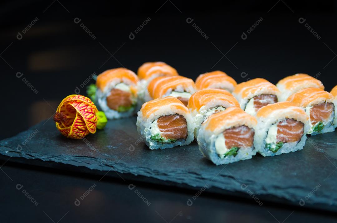 Sushi, cozinha tradicional japonesa. Delicioso Uramaki na placa decorada, fundo preto.