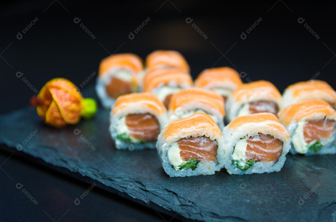 Sushi, cozinha tradicional japonesa. Delicioso Uramaki na placa decorada, fundo preto.