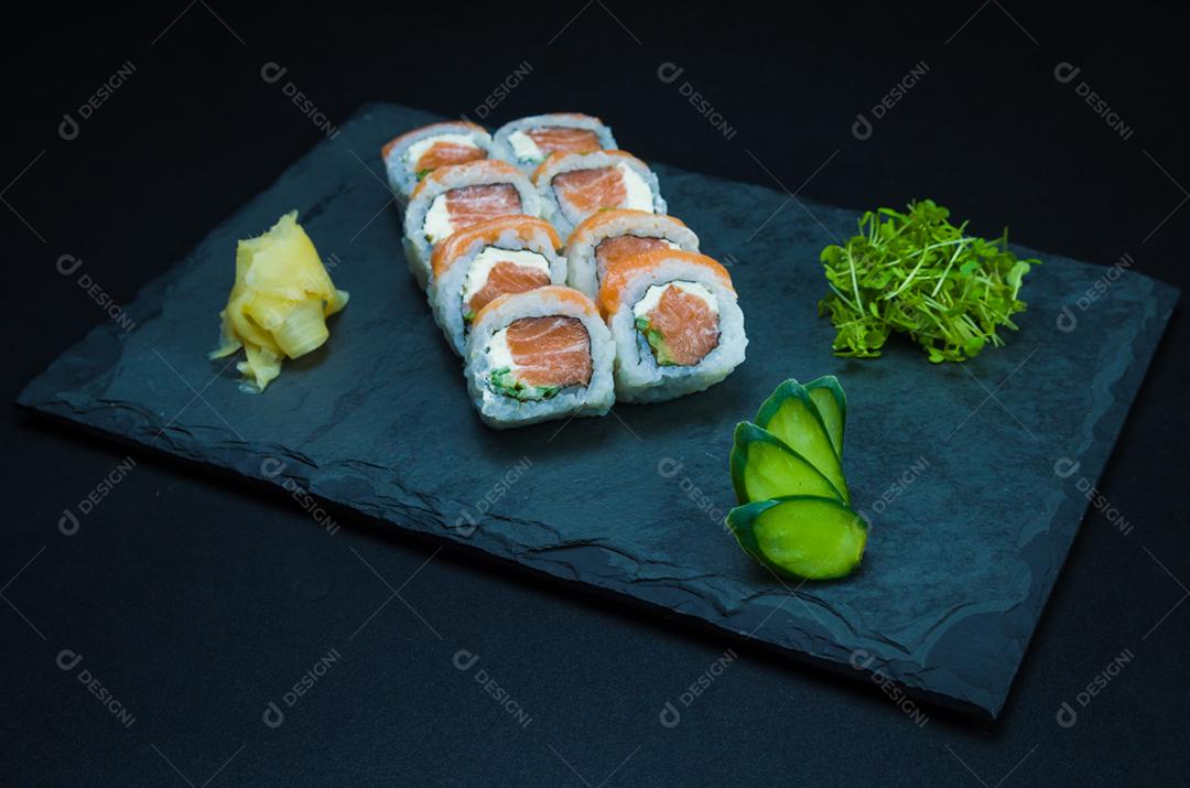 Sushi, cozinha tradicional japonesa. Delicioso Uramaki na placa decorada, fundo preto.