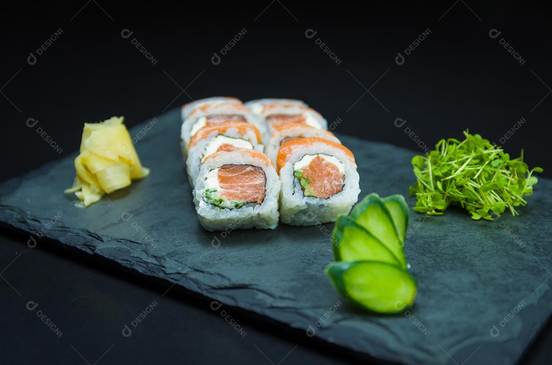 Sushi, cozinha tradicional japonesa. Delicioso Uramaki na placa decorada, fundo preto.