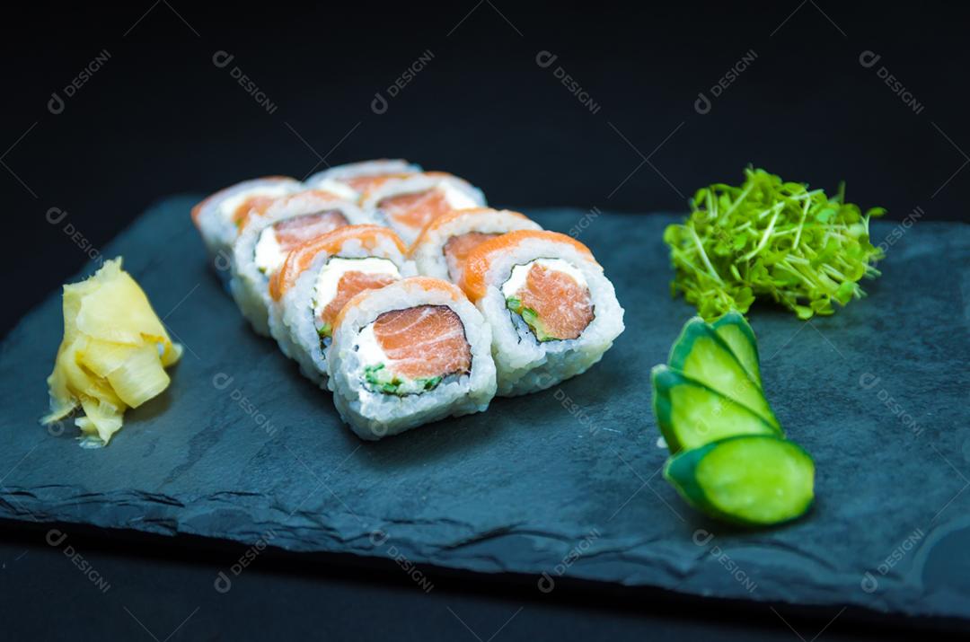 Sushi, cozinha tradicional japonesa. Delicioso Uramaki na placa decorada, fundo preto.