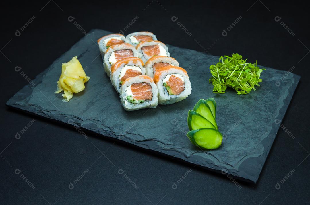 Sushi, cozinha tradicional japonesa. Delicioso Uramaki na placa decorada, fundo preto.