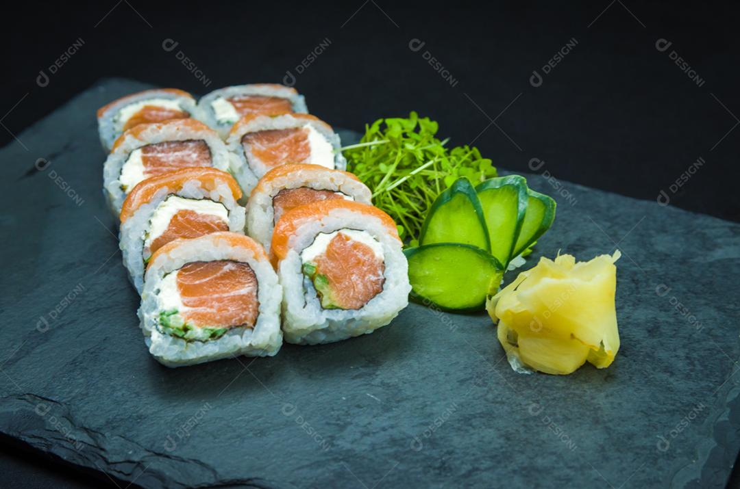 Sushi, cozinha tradicional japonesa. Delicioso Uramaki na placa decorada, fundo preto.