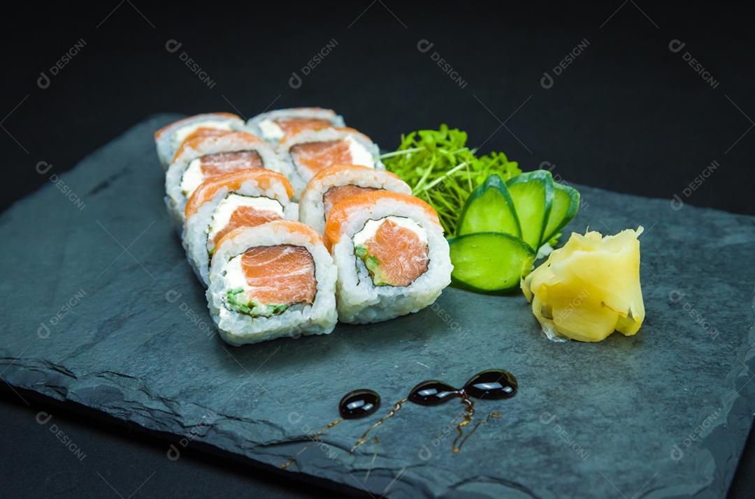 Sushi, cozinha tradicional japonesa. Delicioso Uramaki na placa decorada, fundo preto.