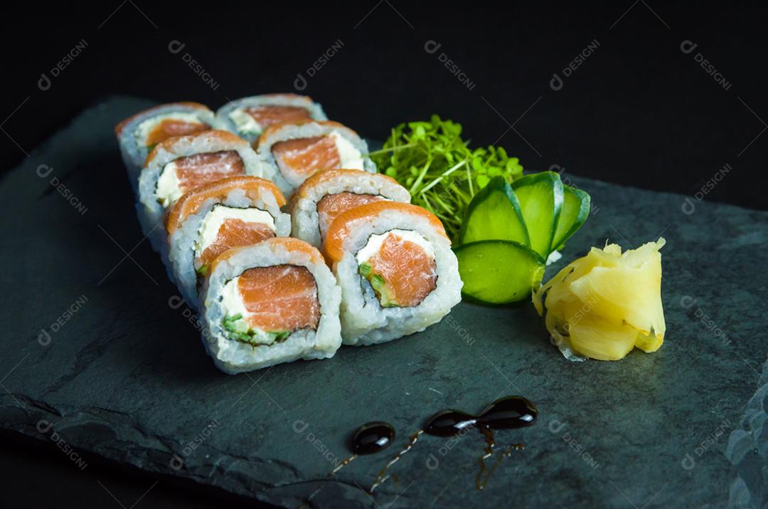 Sushi, cozinha tradicional japonesa. Delicioso Uramaki na placa decorada, fundo preto.