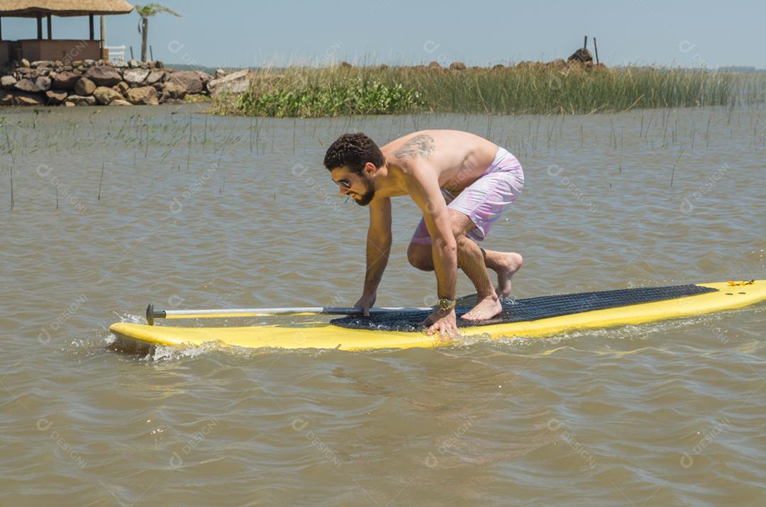 Jovem praticando Stand Up Paddle no lago, placa amarela, remando. Paddleboard.