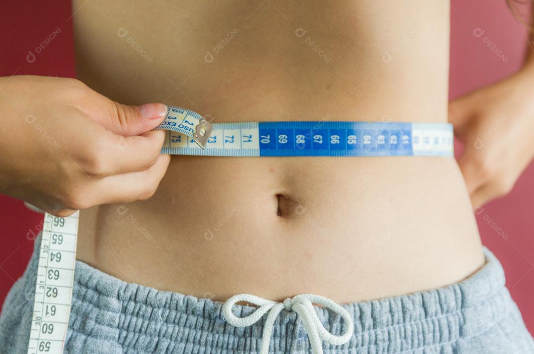 Mulher jovem magra medindo sua cintura fina com uma fita métrica