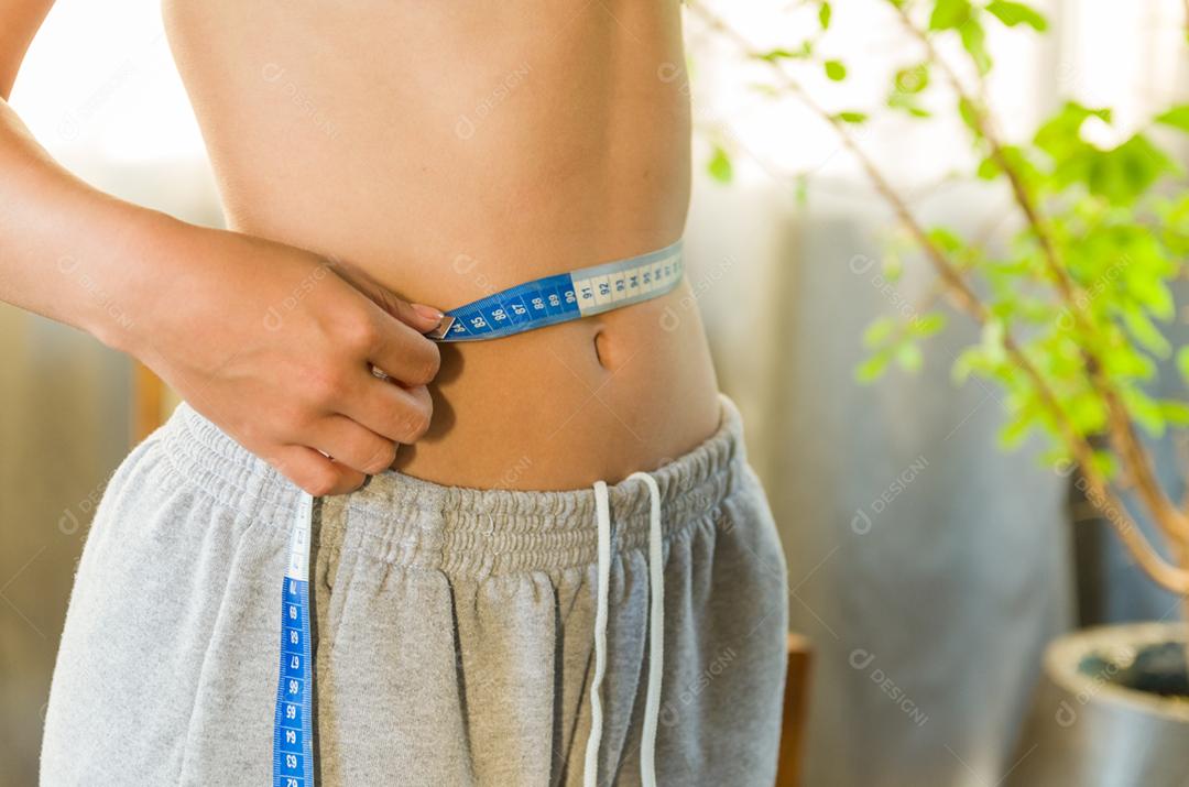 Mulher jovem magra medindo sua cintura fina com uma fita métrica