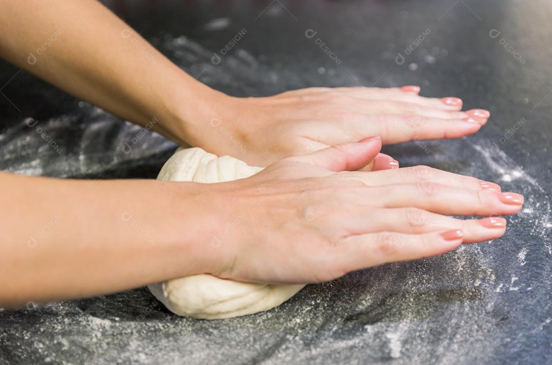Mulher preparando massa de pizza na mesa de granito preto