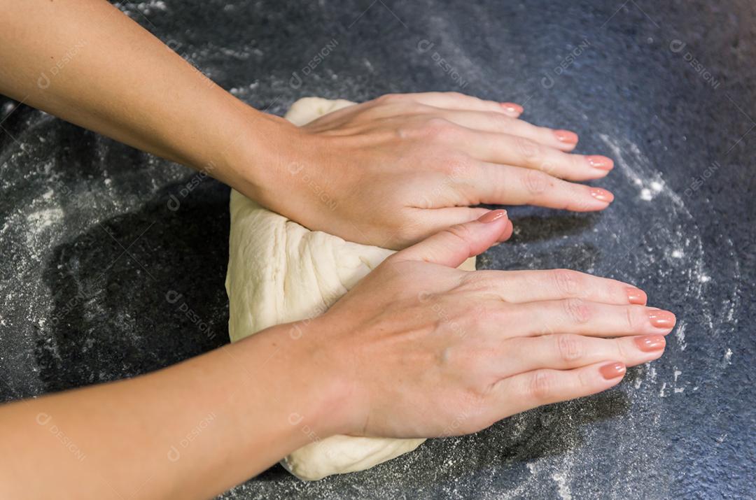 Mulher preparando massa de pizza na mesa de granito preto