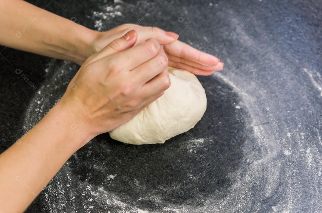 Mulher preparando massa de pizza na mesa de granito preto