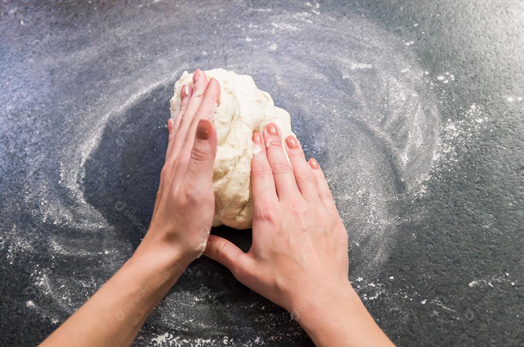 Mulher preparando massa de pizza na mesa de granito preto