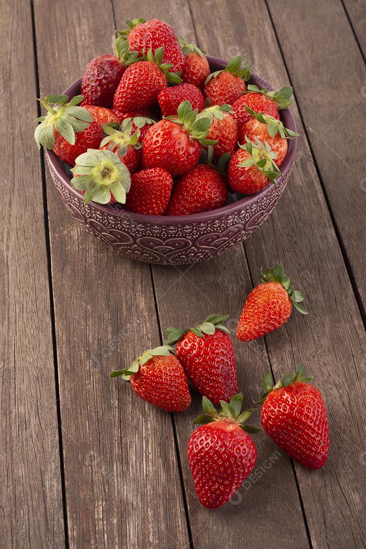 Tigela com morangos sobre mesa de madeira.