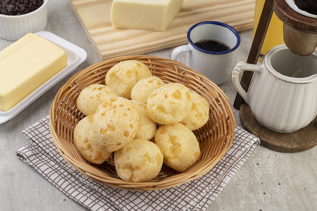 Pão de queijo brasileiro típico em uma cesta, café, manteiga e suco de laranja.