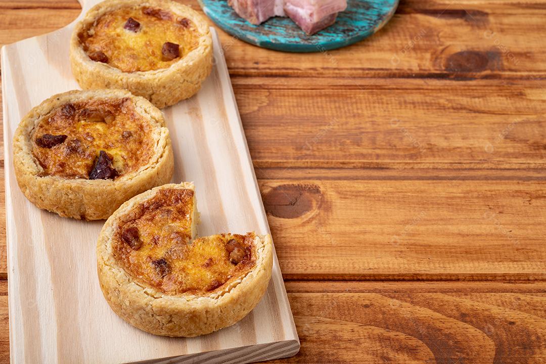 Quiche lorraine caseira sobre tábua de madeira com ingredientes