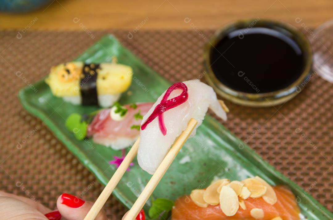 Prato com diferentes tipos de nigirizushi, nigiri com diferentes peixes e um decorado com símbolo de câncer de mama feminino