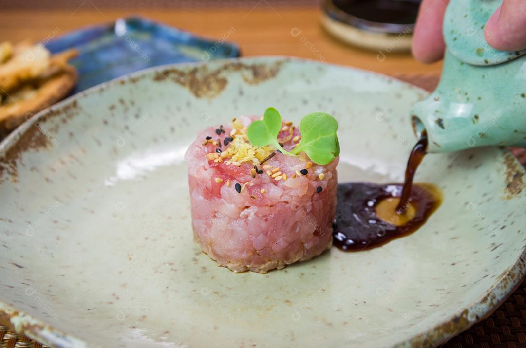 Homem derramando molho de soja em delícias de tártaro de atum em um lindo prato decorado.