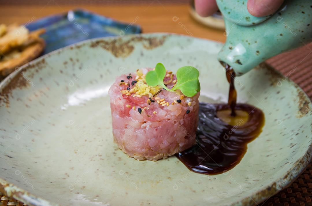 Homem derramando molho de soja em delícias de tártaro de atum em um lindo prato decorado.