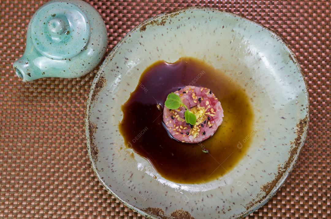 Homem derramando molho de soja em delícias de tártaro de atum em um lindo prato decorado.