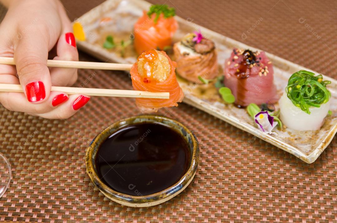 Mulher comendo delicioso sushi gunkan, closeup em pauzinhos