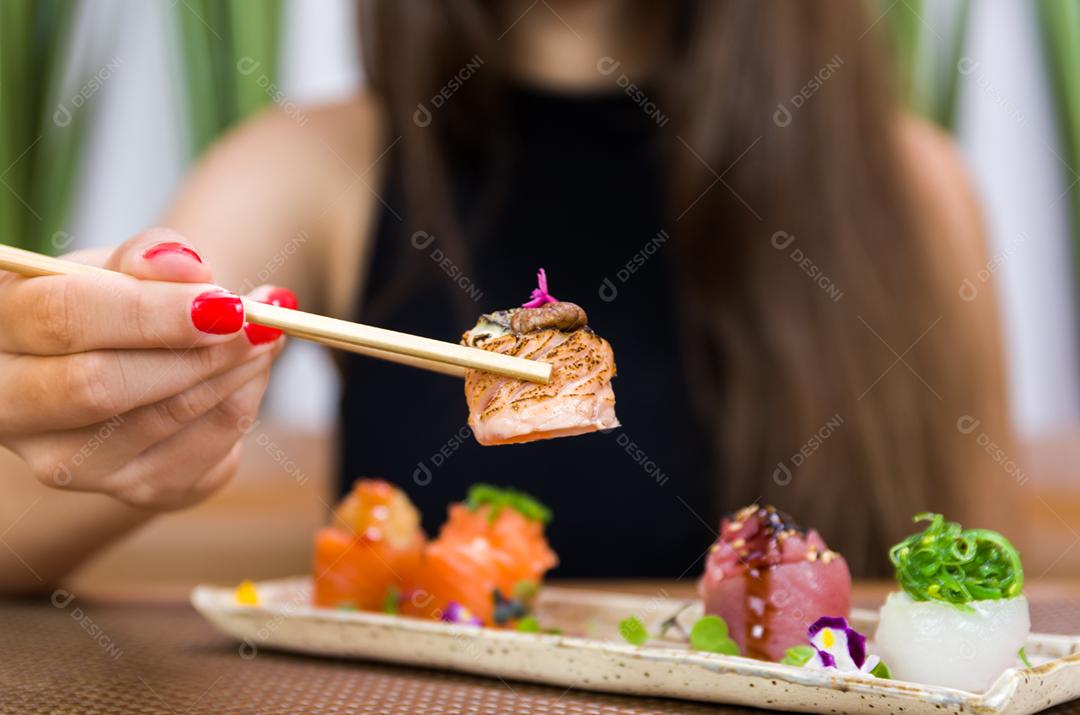 Mulher comendo delicioso sushi gunkan, closeup em pauzinhos