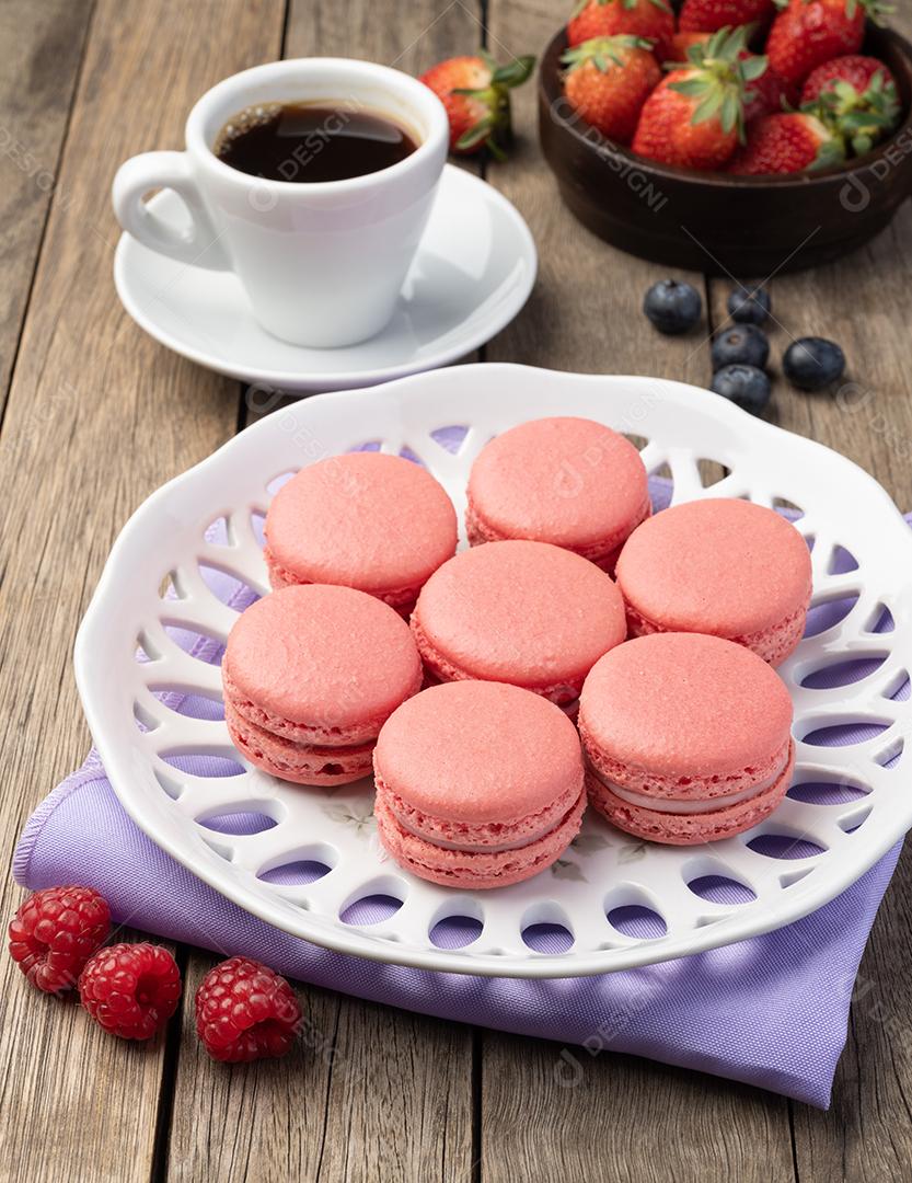 Cranberry macarons in a plate with coffee on a wooden table.
