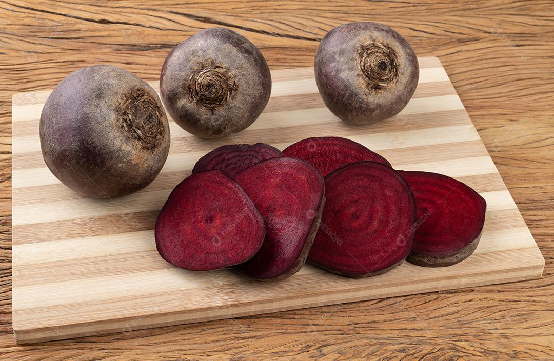 Beterraba crua com beterraba cortada em uma tábua de madeira.