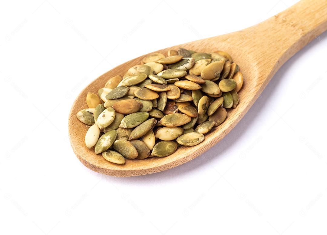 Sementes de abóbora em uma colher isolada sobre fundo branco.