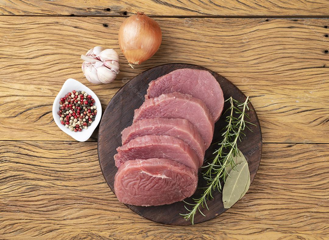 Corte a carne redonda de olho cru sobre a tábua de madeira com temperos.