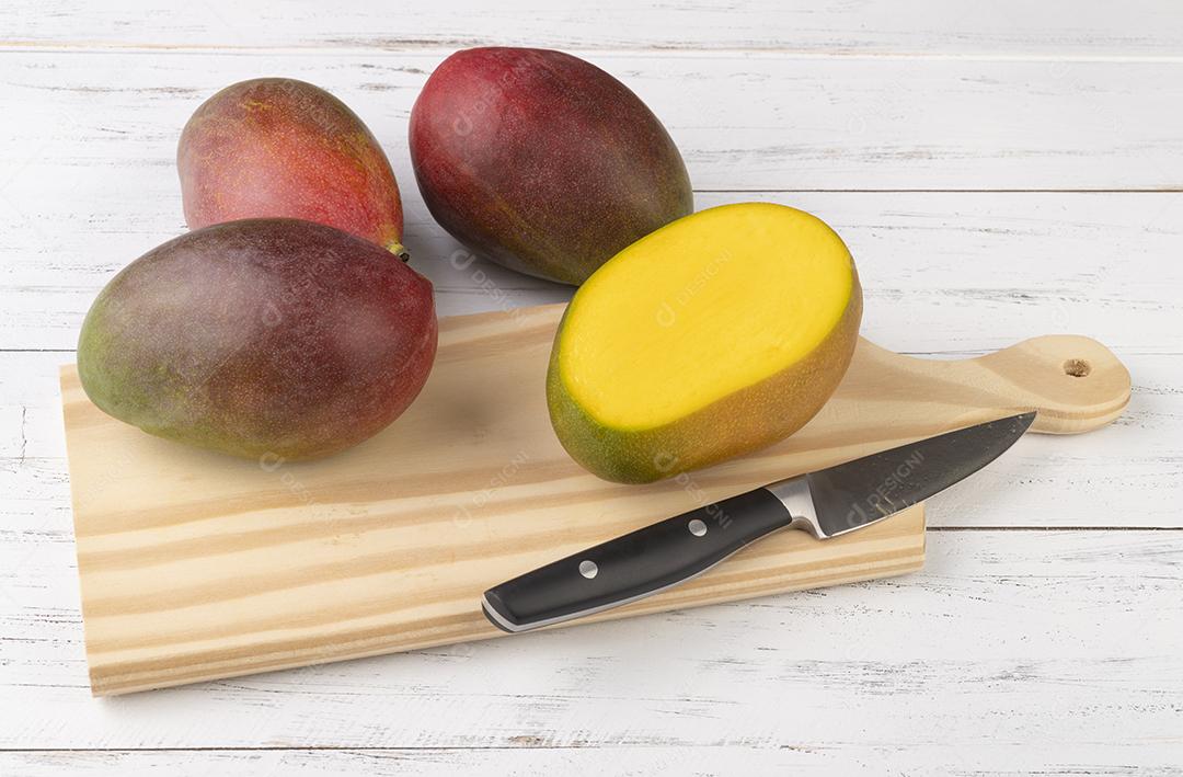 Um grupo de mangas maduras com frutas cortadas sobre tábua de madeira.