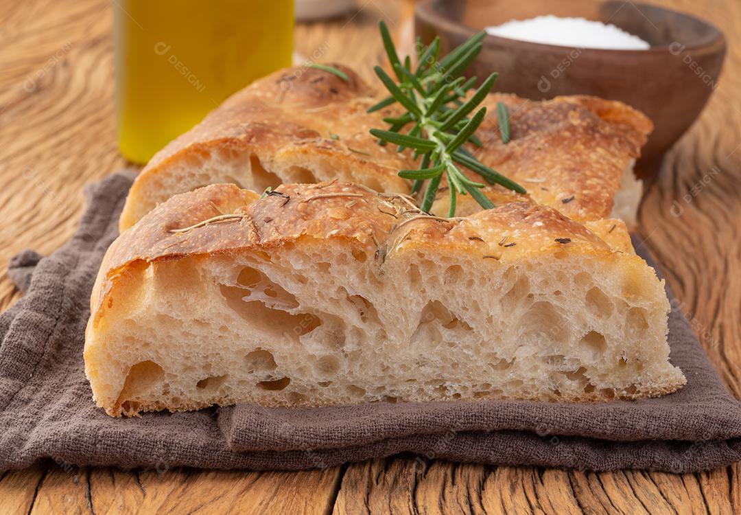 Focaccia caseira com sal, azeite e alecrim sobre mesa de madeira.