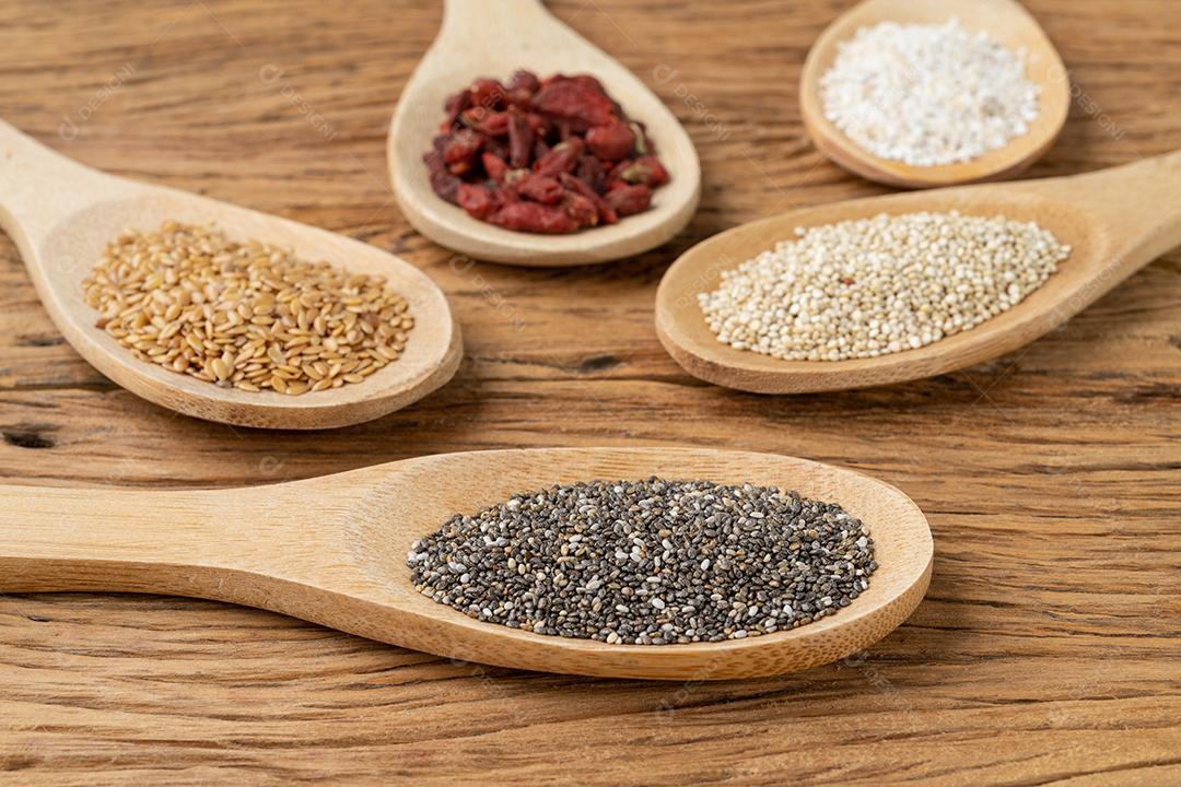 Superalimentos variados em colheres sobre mesa de madeira. Chia, quinoa, aveia, linhaça e goji berry